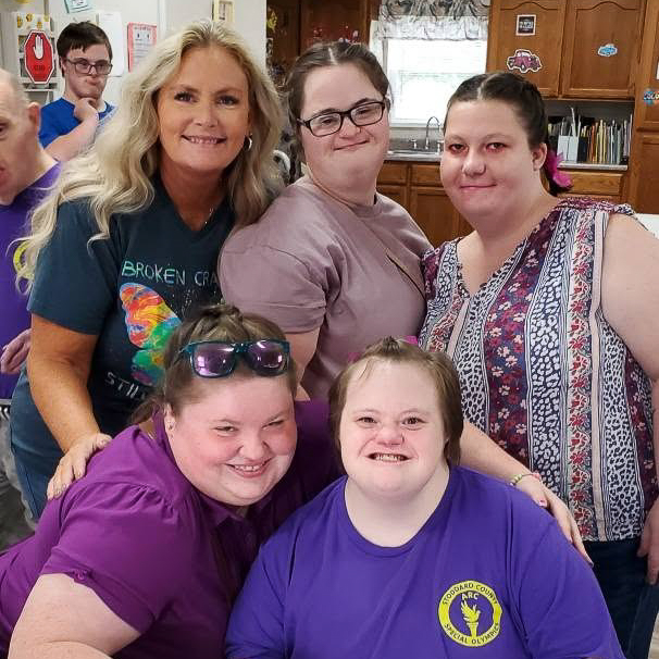 Five women smiling together around a kitchen table.