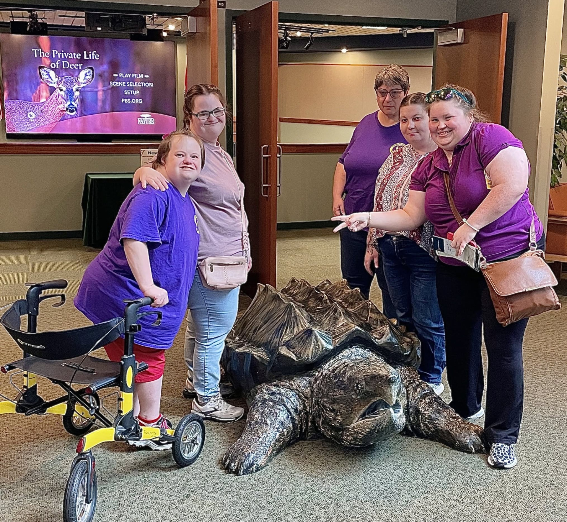 Five people smiling beside a large bronze snapping turtle sculpture indoors.