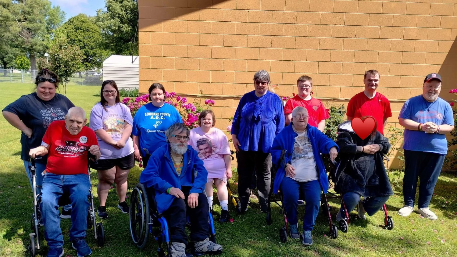 A group of adults and staff smiling outside on a sunny day at a Special Olympics event.