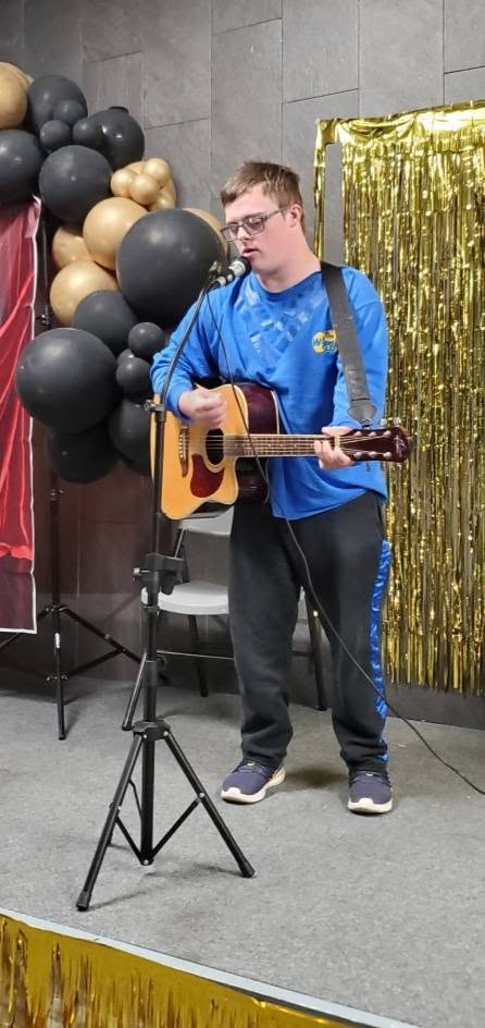 A young man playing guitar and singing at a microphone on a decorated stage.