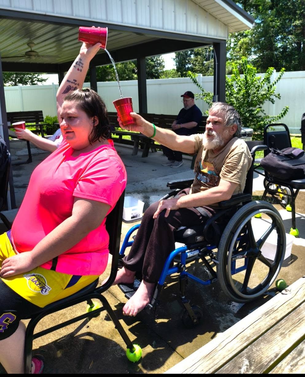 Two friends laughing as they pour cups of water over their heads at an outdoor summer game.